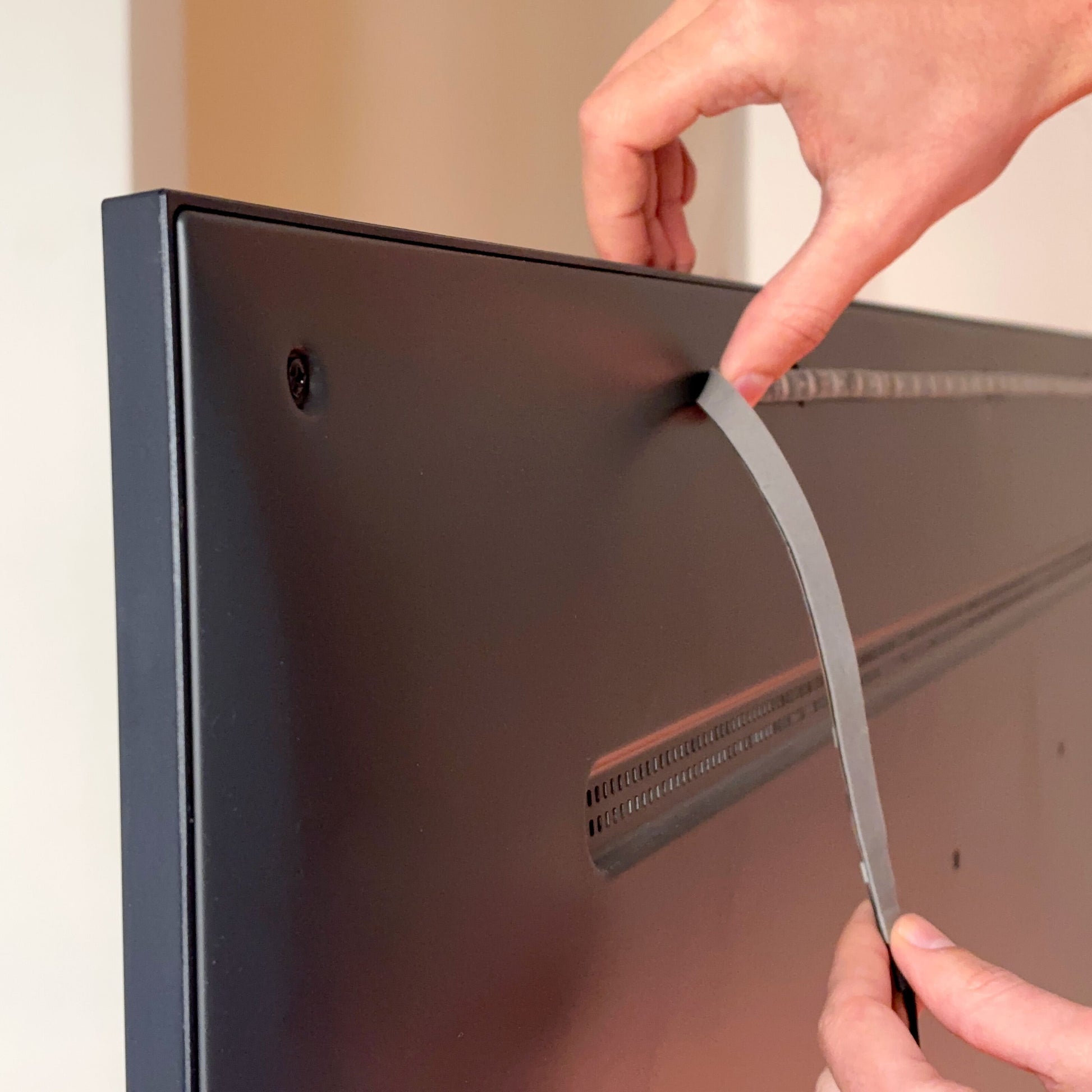 Hænder fjerner beskyttelsesfilm fra sort fladskærms-TV, klar til Wiz WiZ Sync box startpakke 75"-85" RGBIC montering.