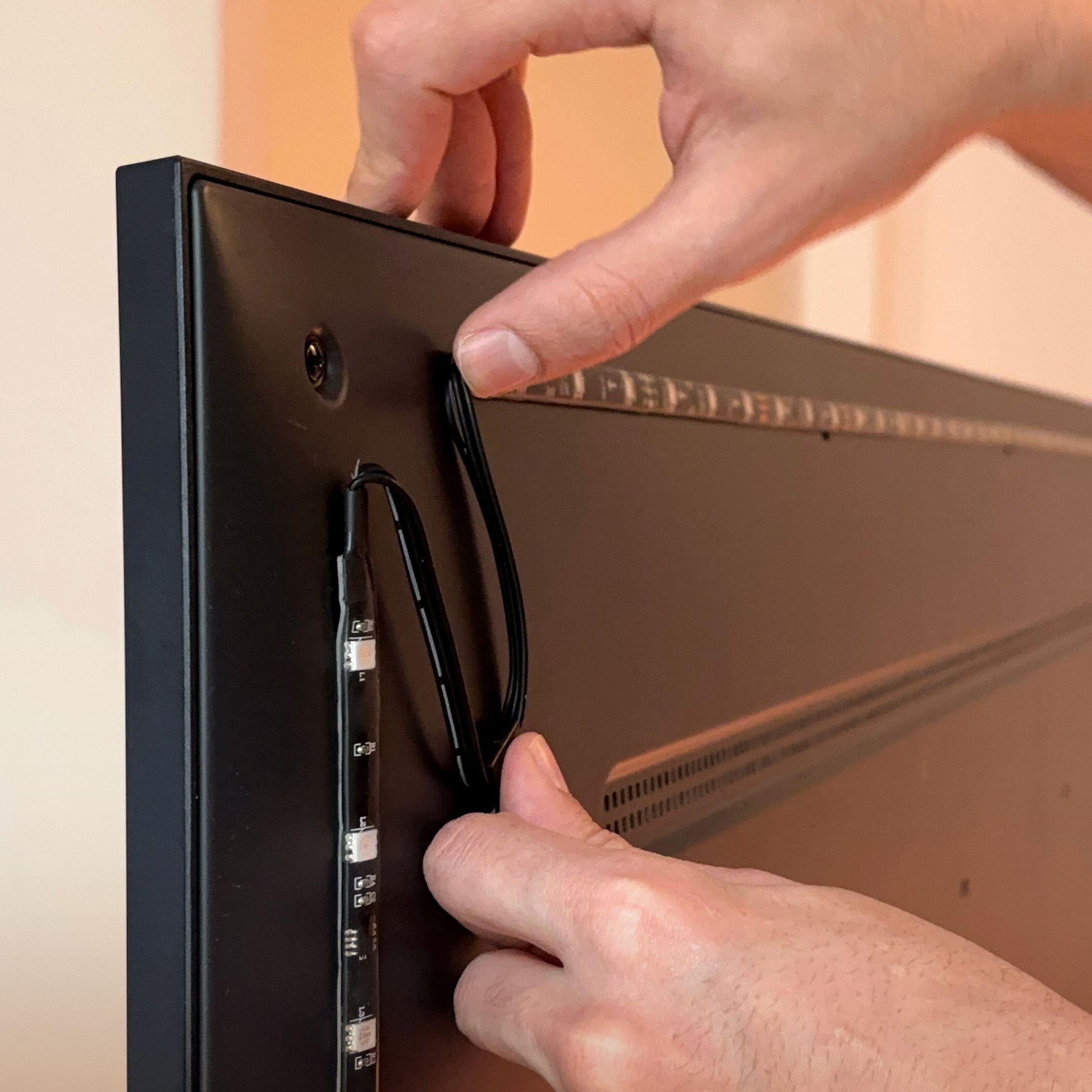 Wiz WiZ Sync box startpakke 75"-85" RGBIC LED strips monteres på bagsiden af fladskærms-TV, kabel og lysbånd håndteres.