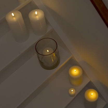 LED Bloklys 3-pak i forskellige størrelser, én med glasholder, tændt og placeret på hvide trapper.