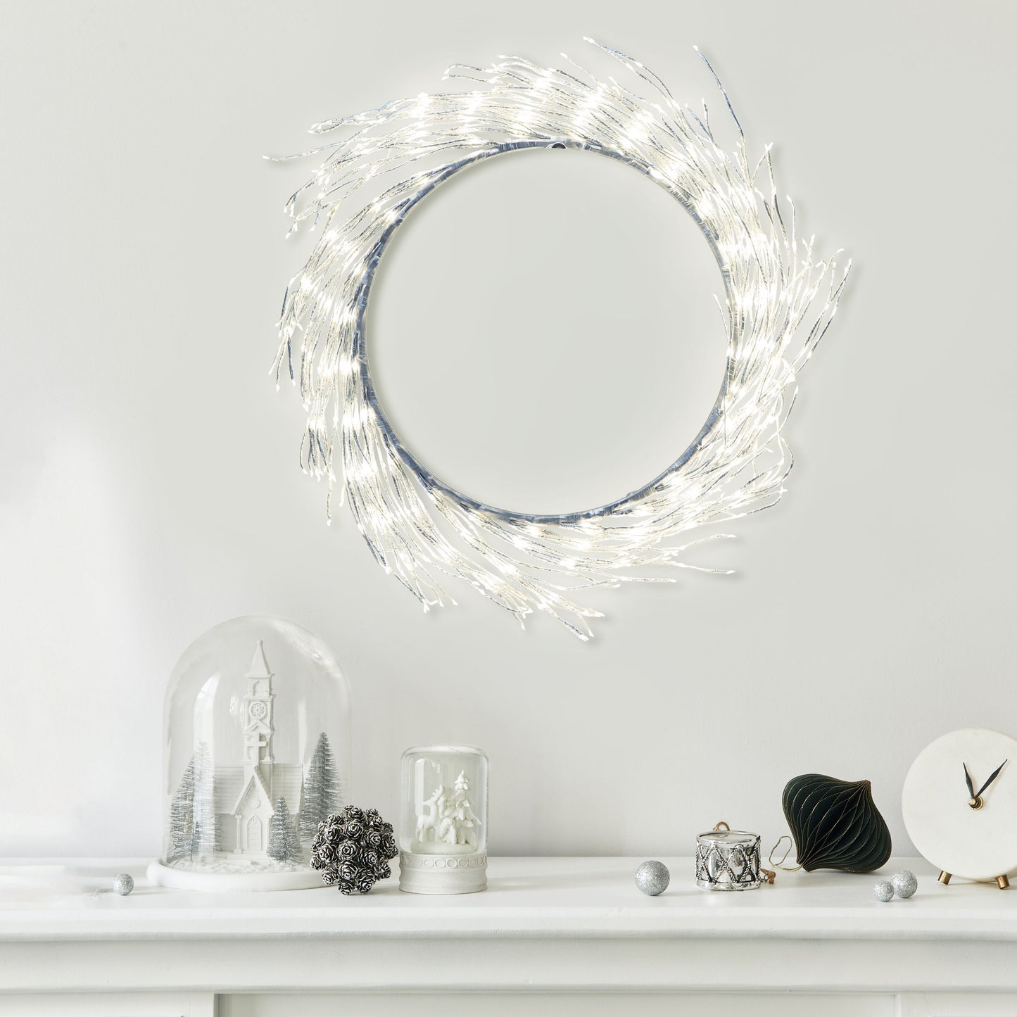 Lyskæde Ring 936 LED Ø50 cm sølv monteret over pejs, synlig med vinterpynt, glaskupler, grankogle og lille ur.