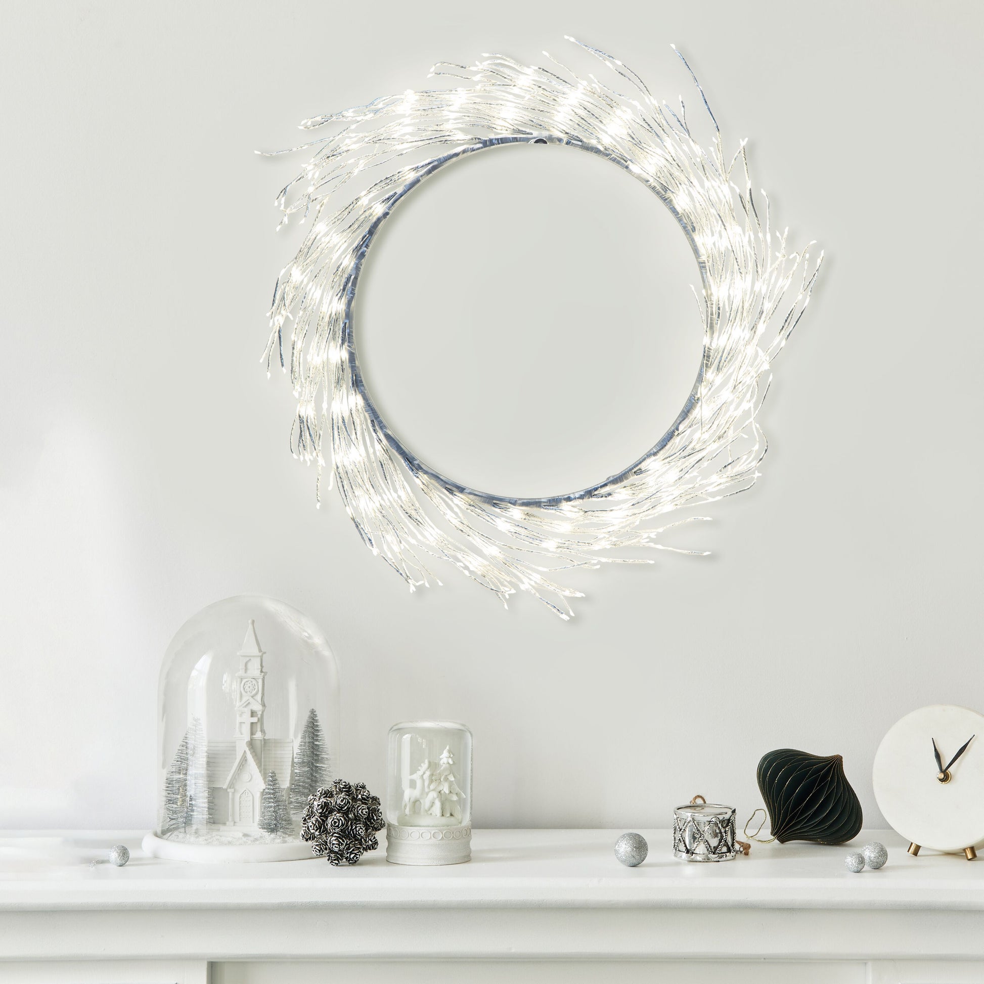Lyskæde Ring 936 LED Ø50 cm sølv monteret over pejs, synlig med vinterpynt, glaskupler, grankogle og lille ur.