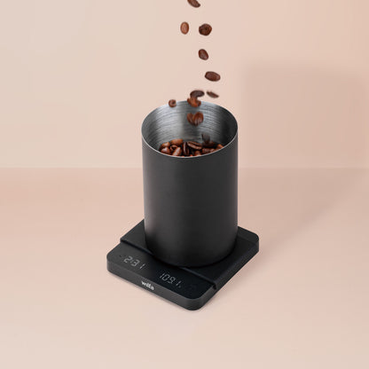 Wilfa Uni Mini kaffevægt med LED-display, sorte kaffebønner i sort metalkop, beige baggrund.