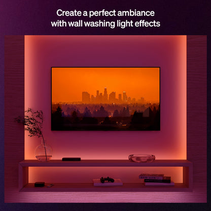 Philips Hue Flux LED-strip 10m RGBW bag tv, synlig hylde med controller, bøger, dekoration og glasvase med grene.
