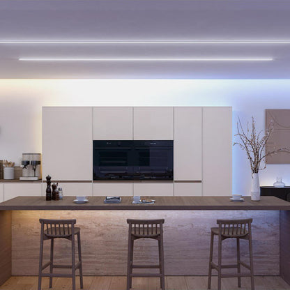 Philips Hue OmniGlow smart lysliste dæmpbar belysning monteret på hvide køkkenskabe, træø og glasvase med grene.