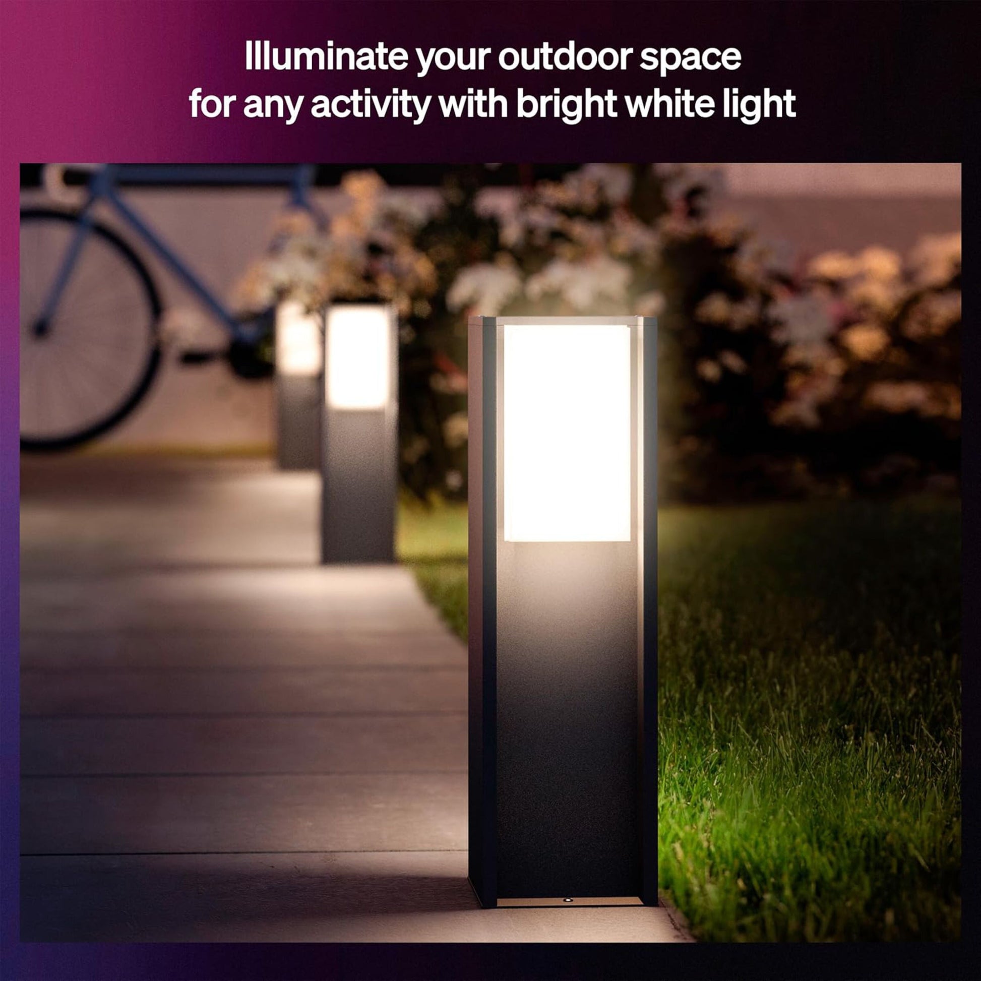 Philips Hue Turaco pullertlamper antracit lyser havegang op i farverig belysning, græs, planter og cykel synlige.