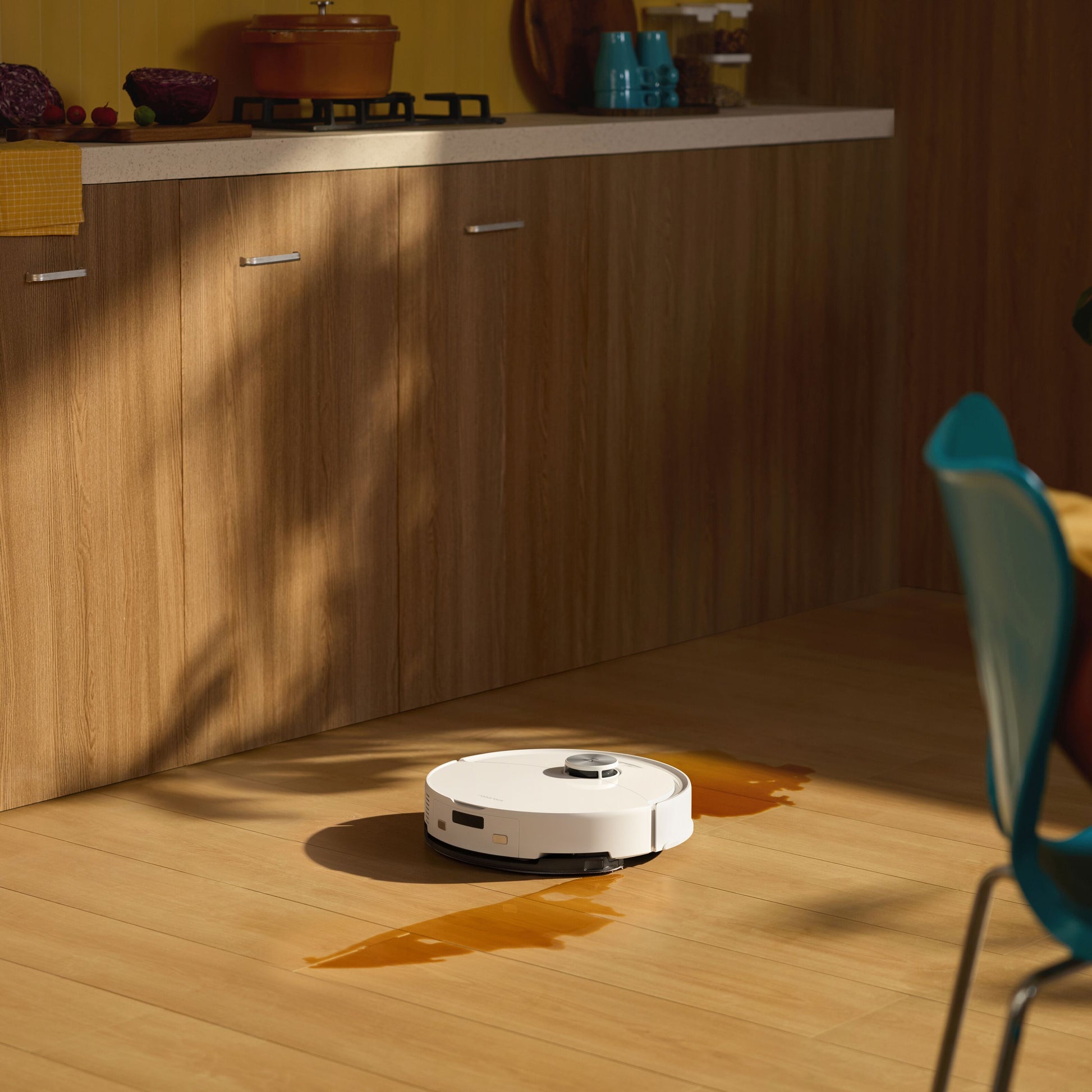 Roborock Q10 VF+ robotstøvsuger hvid med automatisk tømning og ladestation rengør spildt væske på trægulv i køkken.