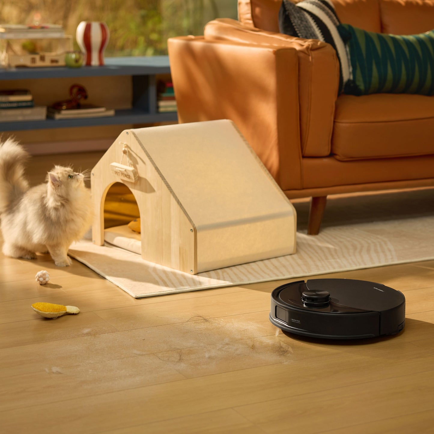 Roborock Q10 VF+ robotstøvsuger med ladestation sort gør gulvet rent ved sofagruppe, kat og lille træ kæledyrshus ses.