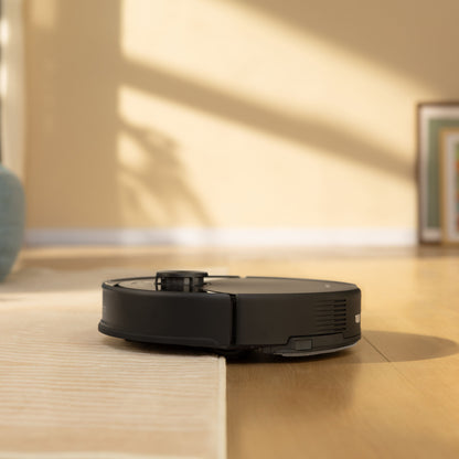 Roborock Q10 VF+ robotstøvsuger sort med ladestation på lyst trægulv, beige væg, automatisk tømning.