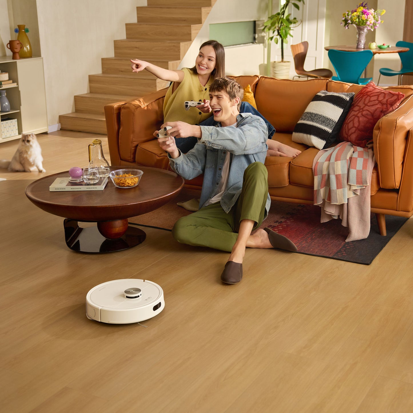 Roborock Q7 TF+ robotstøvsuger hvid med ladestation på trægulv ved brun sofa, kat ved trappe i baggrunden.