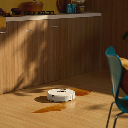 Roborock Q7 TF+ robotstøvsuger med ladestation fjerner orange væskespild på trægulv ved træskabe og blå stol.
