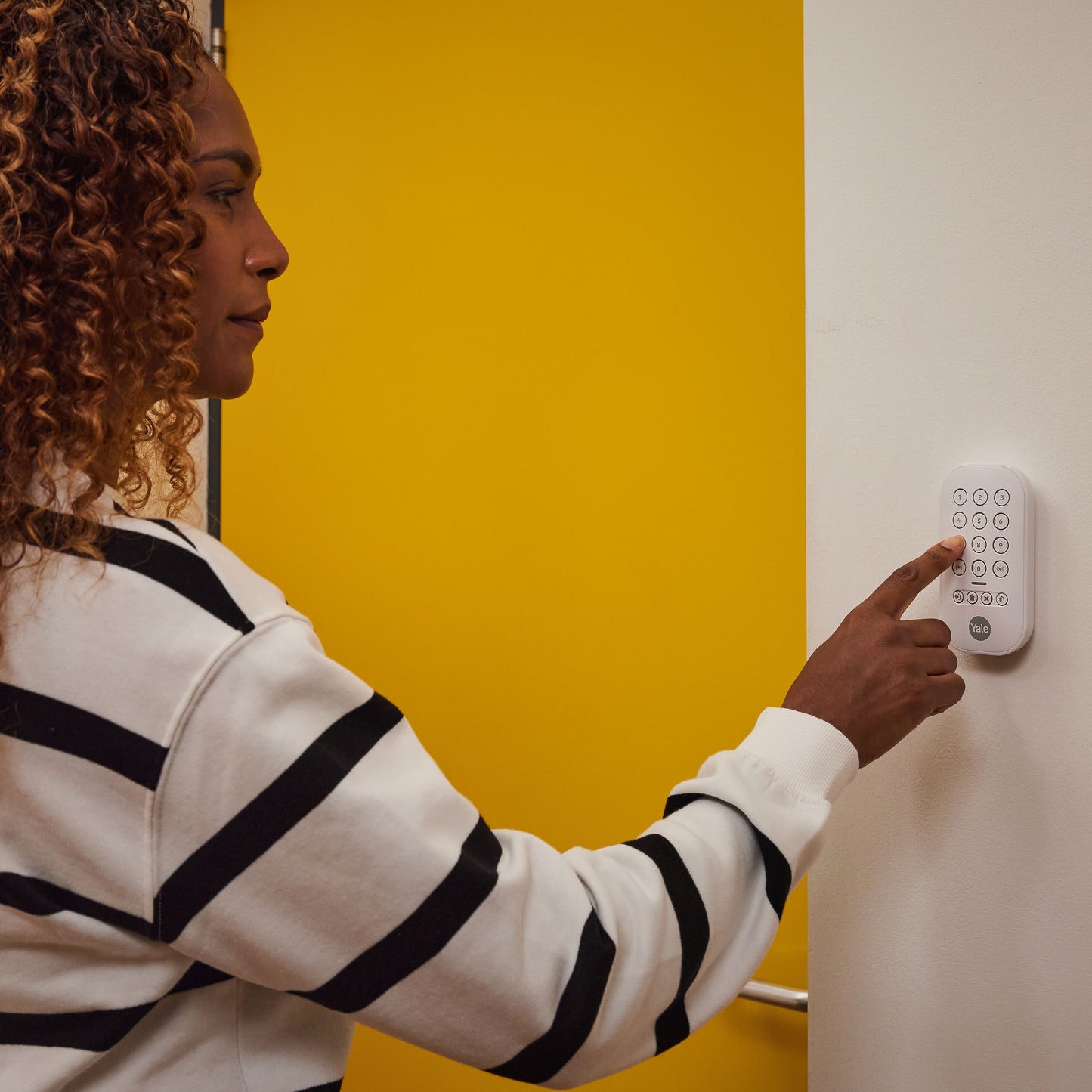 Yale Alarmknap sæt monteret på væg-nøglepanel ved gul dør, vises i brug, detalje af knap og panel.