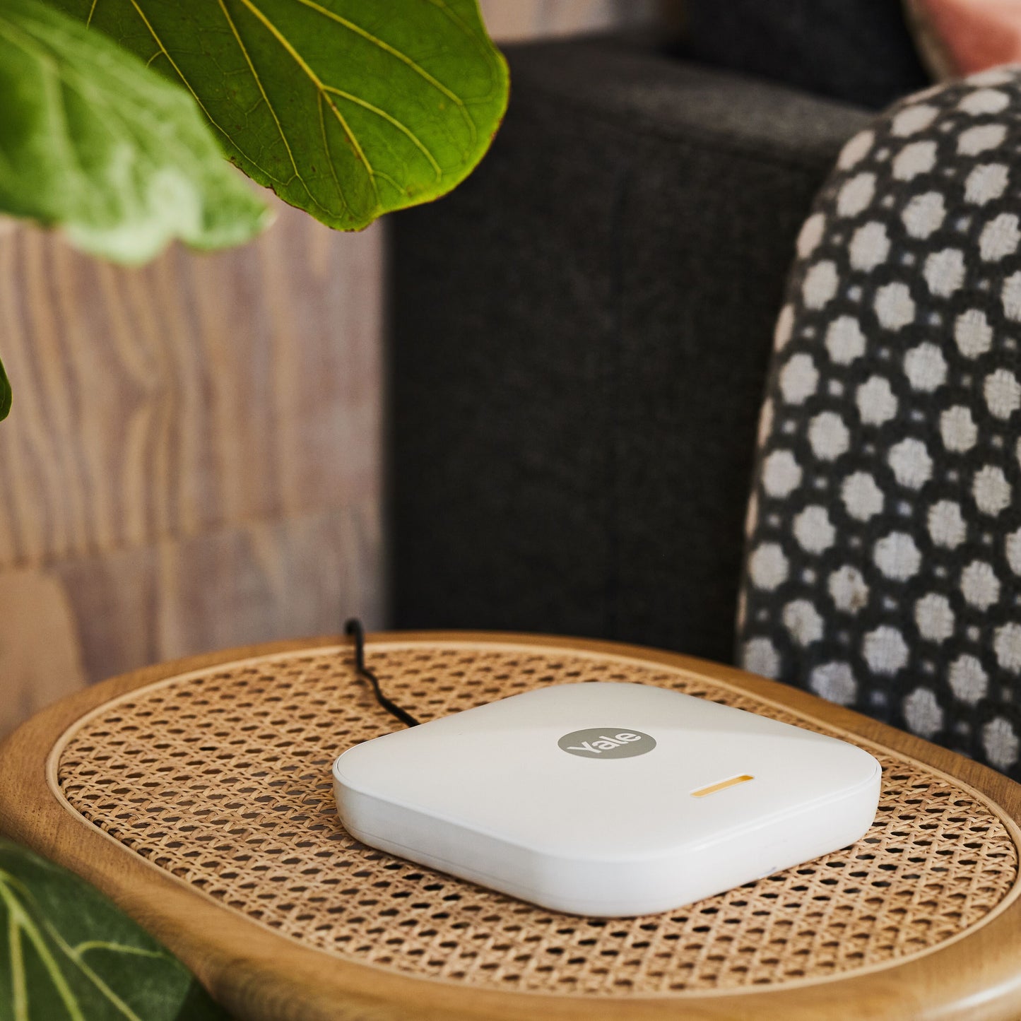 Yale Startalarmkit+ smart home alarm med bevægelsesdetektorer på rattanbord ved siden af plante og tæppe.
