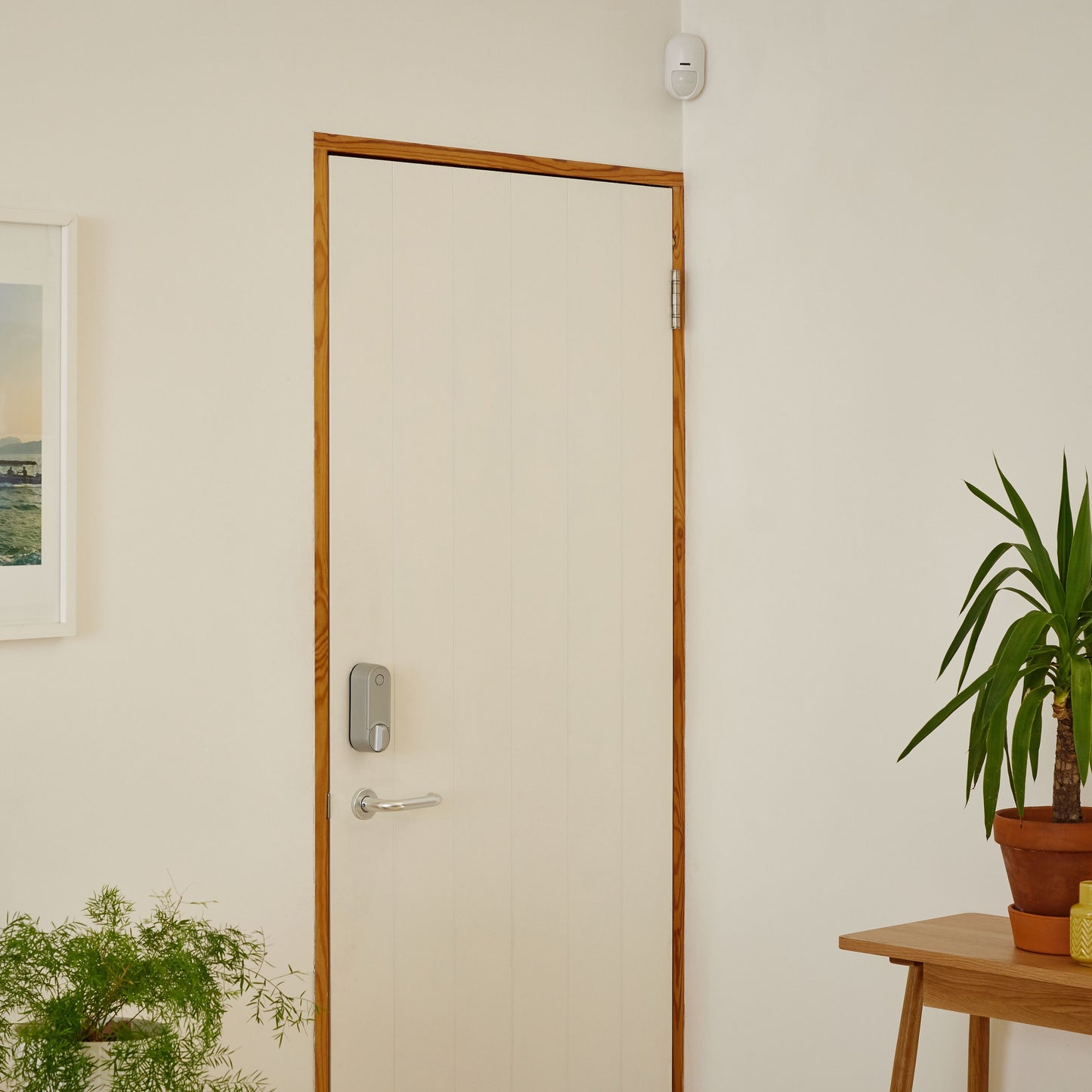 Yale smartlås og sølvhåndtag på lys dør, Yale Startalarmkit+ monteret over døren, beige væg.