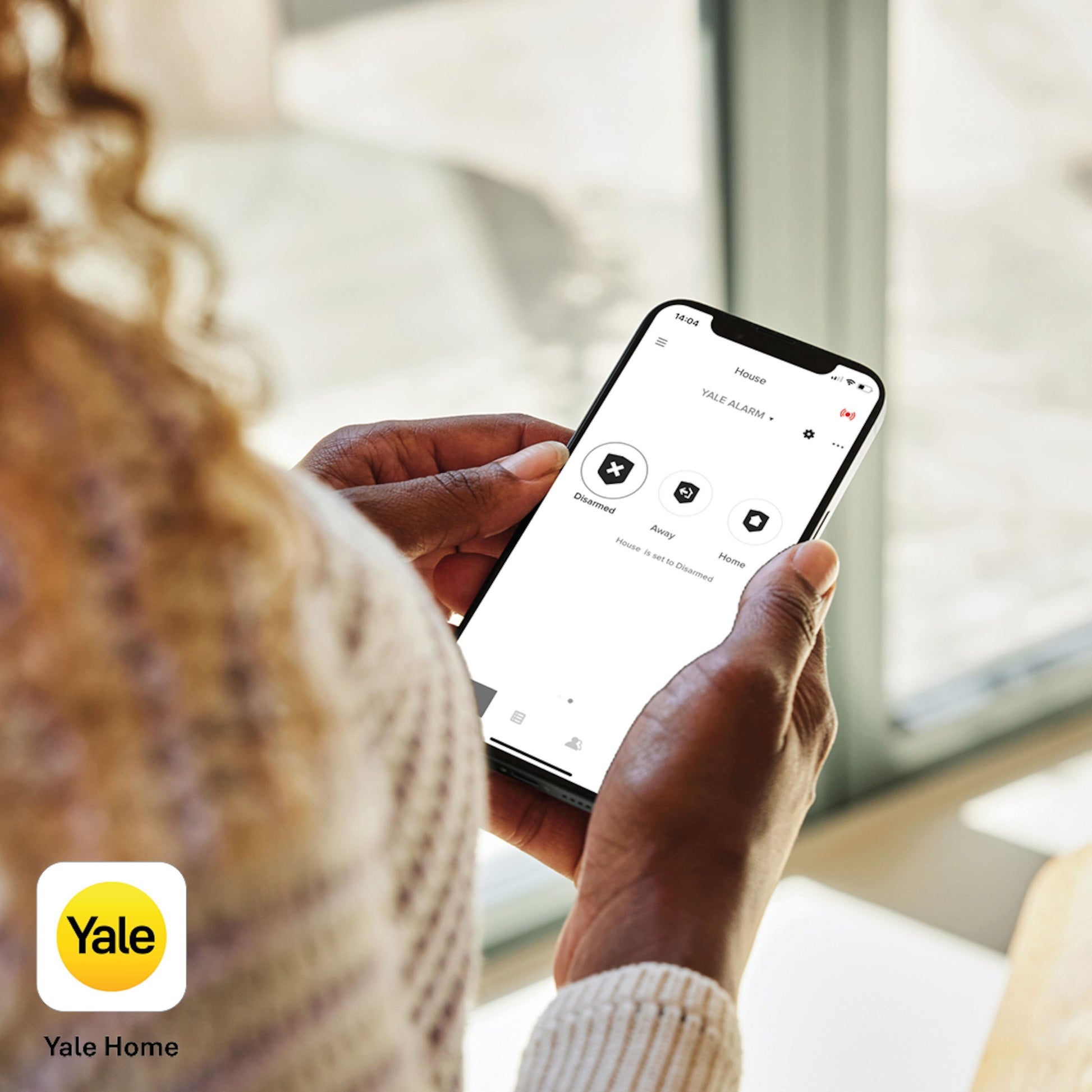 Smartphone med Yale Home app åben, viser sikkerhed, enheder og rum. Yale Røgalarm logo synligt i hjørnet.