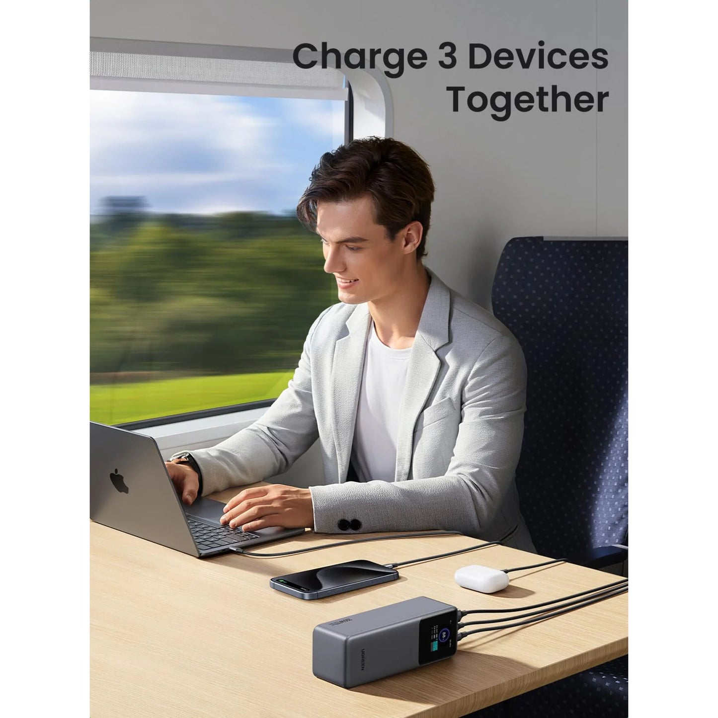 Ugreen Nexode 25000 mAh powerbank oplader mobil og øretelefoner via laptop på bord i tog, oplader 3 enheder sammen vises.