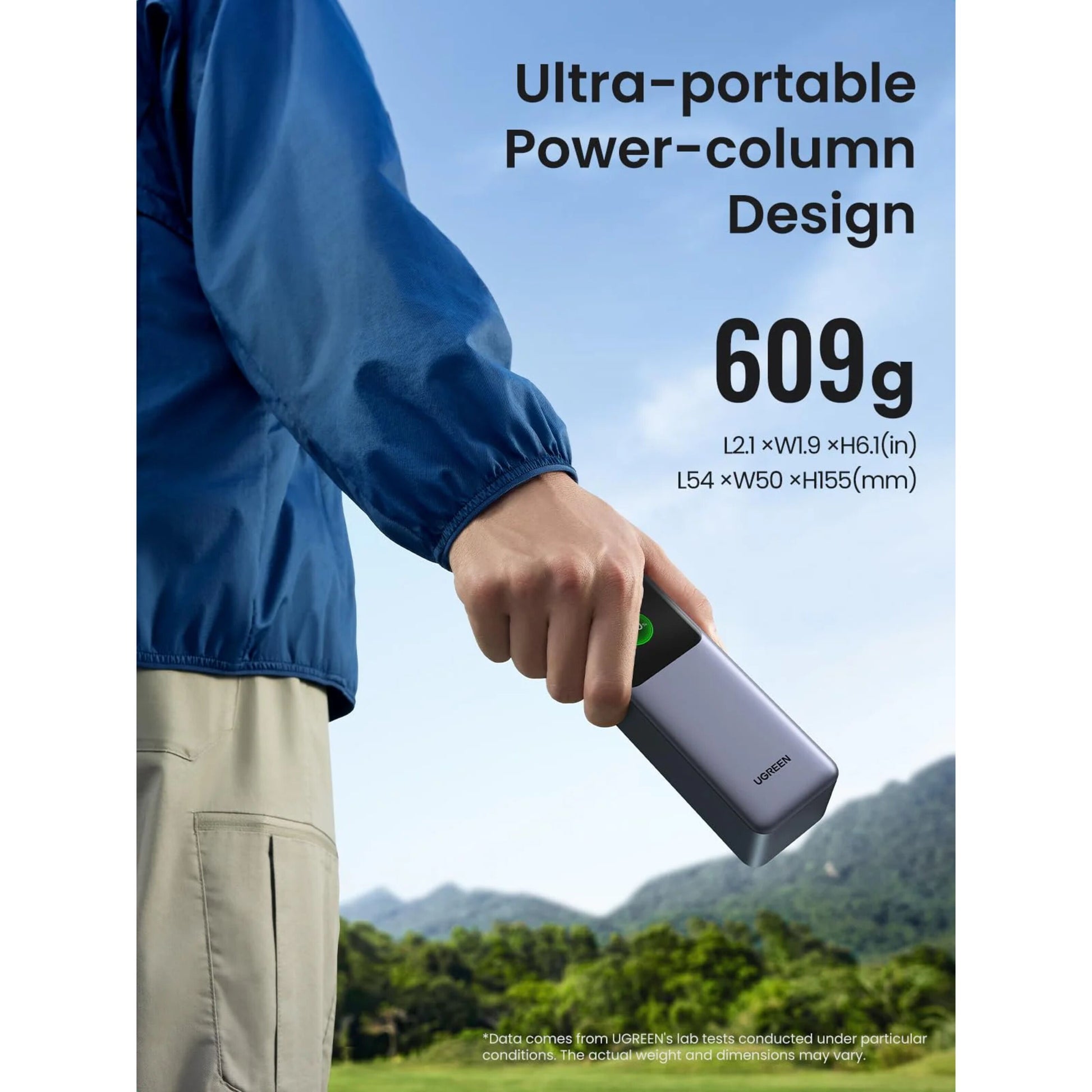 Ugreen Nexode 25.000 mAh powerbank, blå, kompakt, 609g, 140W opladning, ses i hånd foran udendørs baggrund.