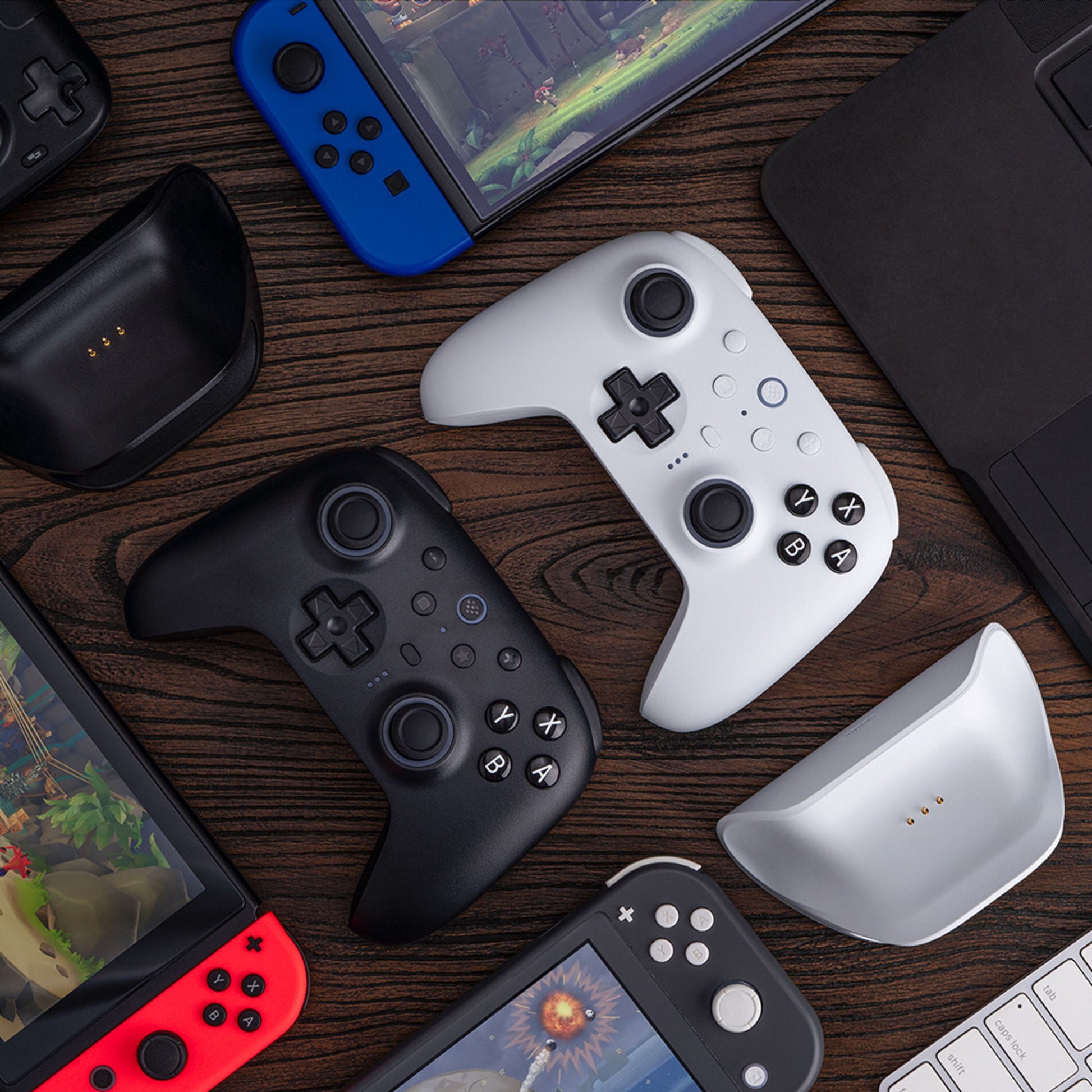 8Bitdo Ultimate 2 Bluetooth Controller Hvid, gaming controllere, håndholdte konsoller og laptopdele på mørkt træbord.