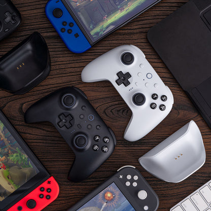 8Bitdo Ultimate 2 Bluetooth Controller Hvid, gaming controllere, håndholdte konsoller og laptopdele på mørkt træbord.