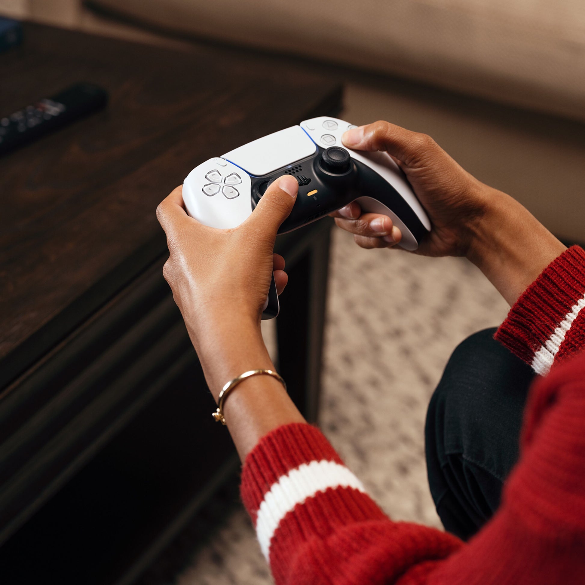 Sony PlayStation 5 Slim Digital Edition 825 GB controller holdt i hånd, rød/hvid stribet sweater, træbord med fjernbetjening.