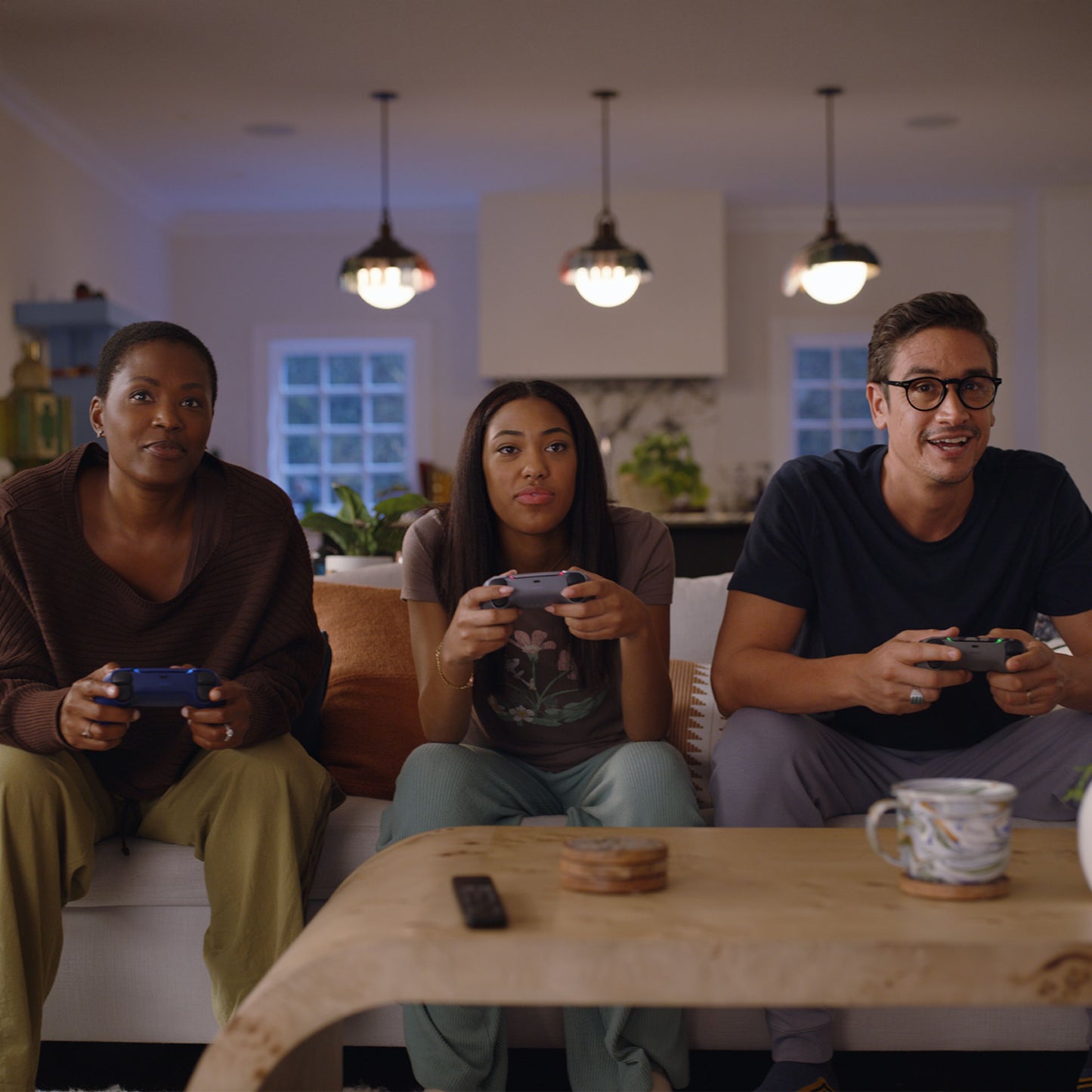PlayStation 5 Slim Digital Edition 825GB konsol i brug, tre personer med controllere, kaffebord med krus og fjernbetjening.