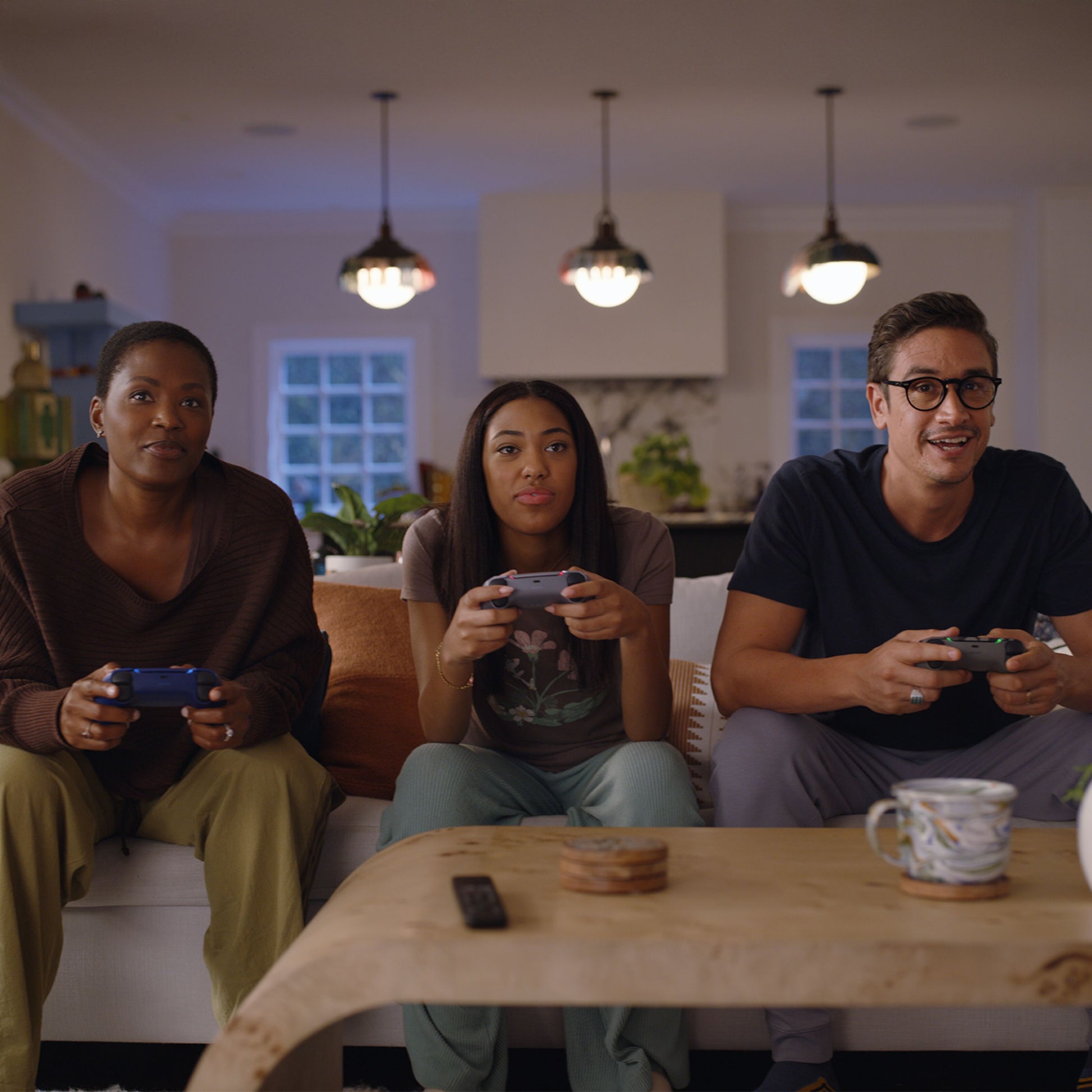 PlayStation 5 Slim Digital Edition 825GB konsol i brug, tre personer med controllere, kaffebord med krus og fjernbetjening.