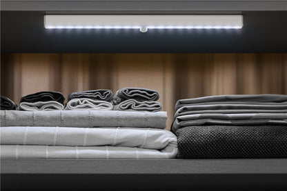 Goobay LED-underkabinetlampe med bevægelsessensor 33cm lyser hylde med håndklæder i lyse og mørke nuancer.