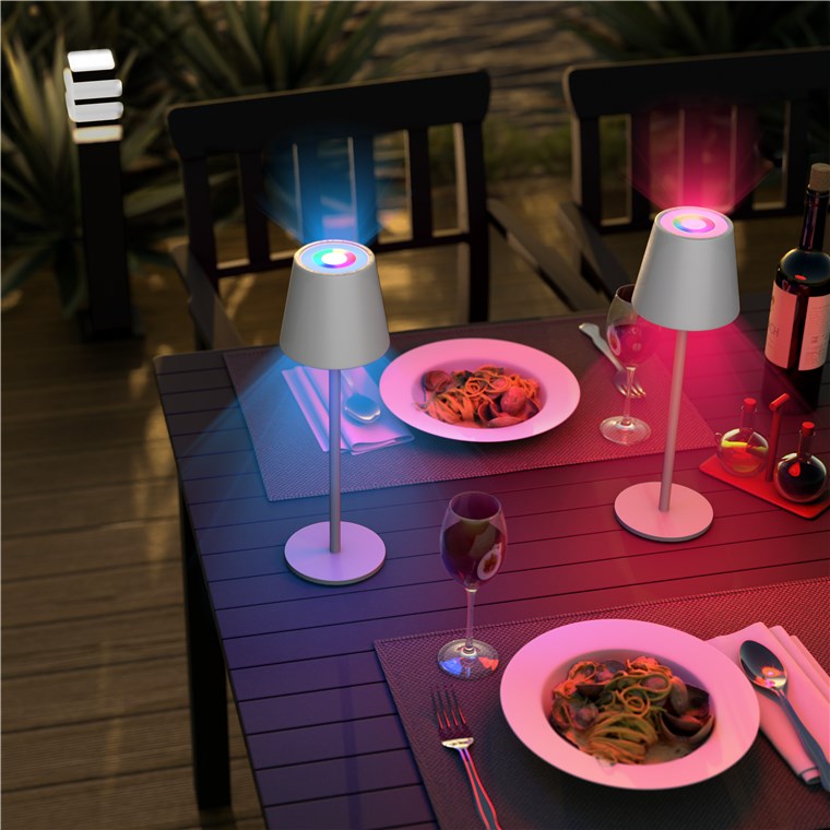 Goobay Trådløs LED-bordlampe RGBW hvid lyser i blå og pink på bord med pasta og vin udendørs.
