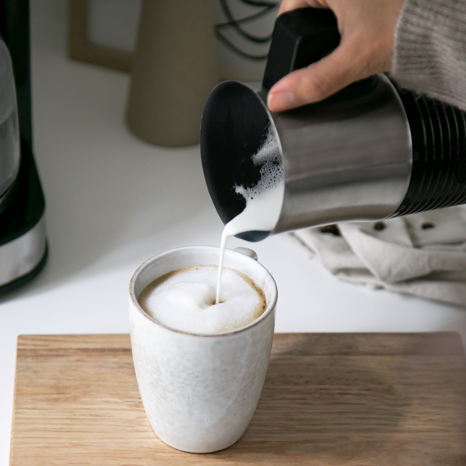 Champion mælkeskummer MS210 hælder fugtig mælk i kaffekop med skum på træbræt.