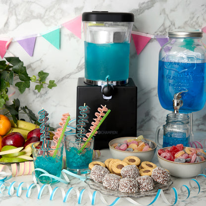 Champion Slush Ice Maskine 1L sort på bord med blå drinks i glas med spiralstrå, slik, kiks, lamingtons og frisk frugt.