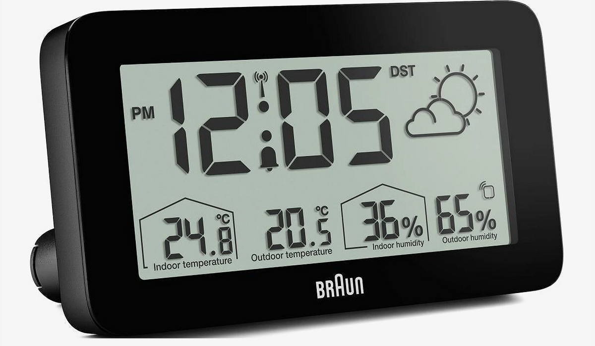 BRAUN digital vejrstation med baggrundsbelysning, LCD-display viser kl. 12:05, temperatur og luftfugtighed inde/ude, ikon for delvist overskyet.