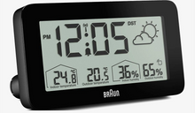 BRAUN digital vejrstation med baggrundsbelysning, LCD-display viser kl. 12:05, temperatur og luftfugtighed inde/ude, ikon for delvist overskyet.
