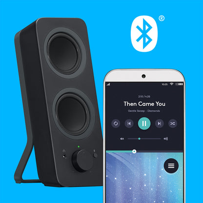 Logitech Z207 Bluetooth-højttalere med to højttalerenheder, lydstyrkeknap og hovedtelefonstik, parret med en smartphone.