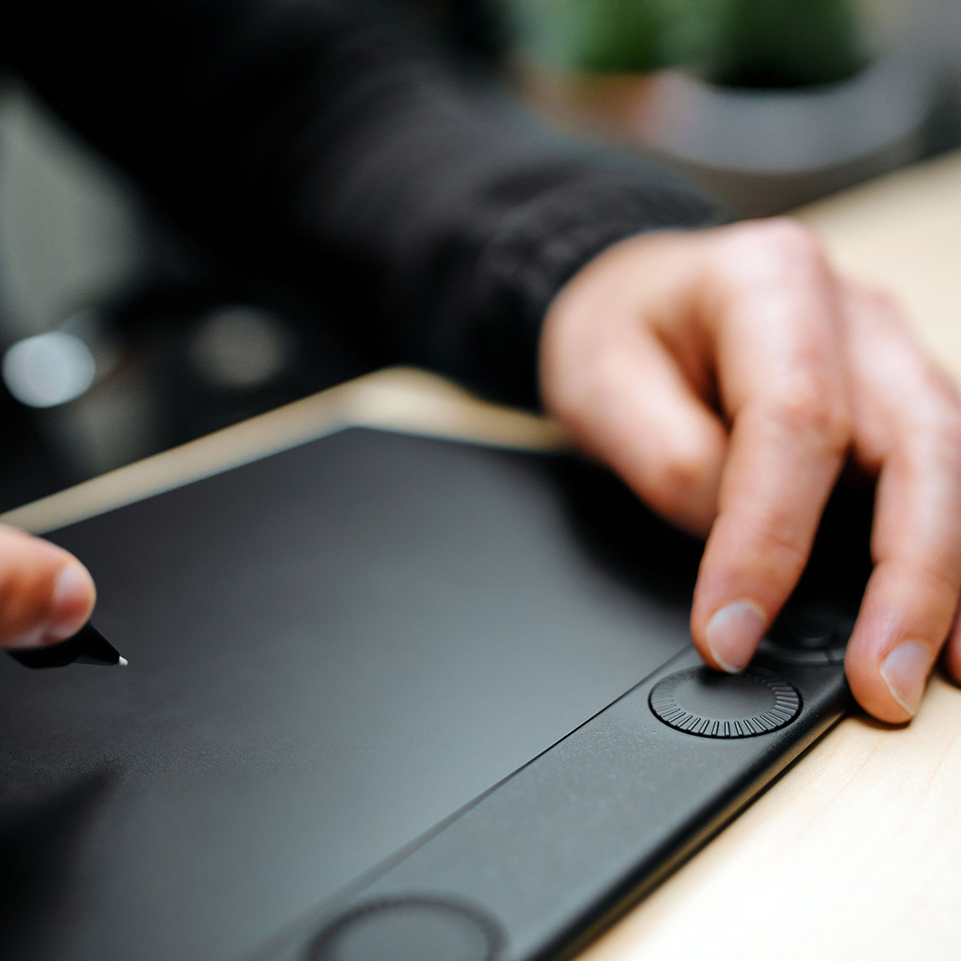 Wacom Intuos Pro lille tegneplade 187 x 105 mm med stylus i hånd og anden hånd på tablet-dial ved lyst træskrivebord.