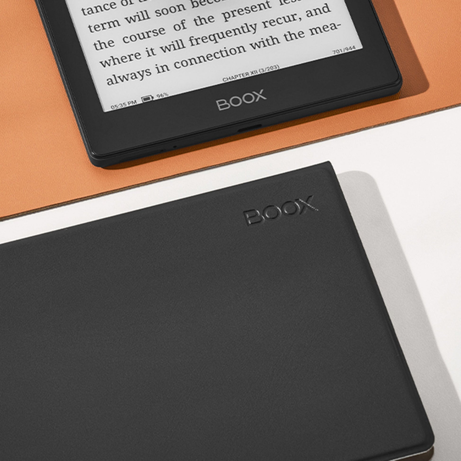 Boox Onyx Gå 6 e-boglæser med magnetisk etui, visning af bogtekst, ved siden af lukket sort Boox Onyx enhed på orange flade.