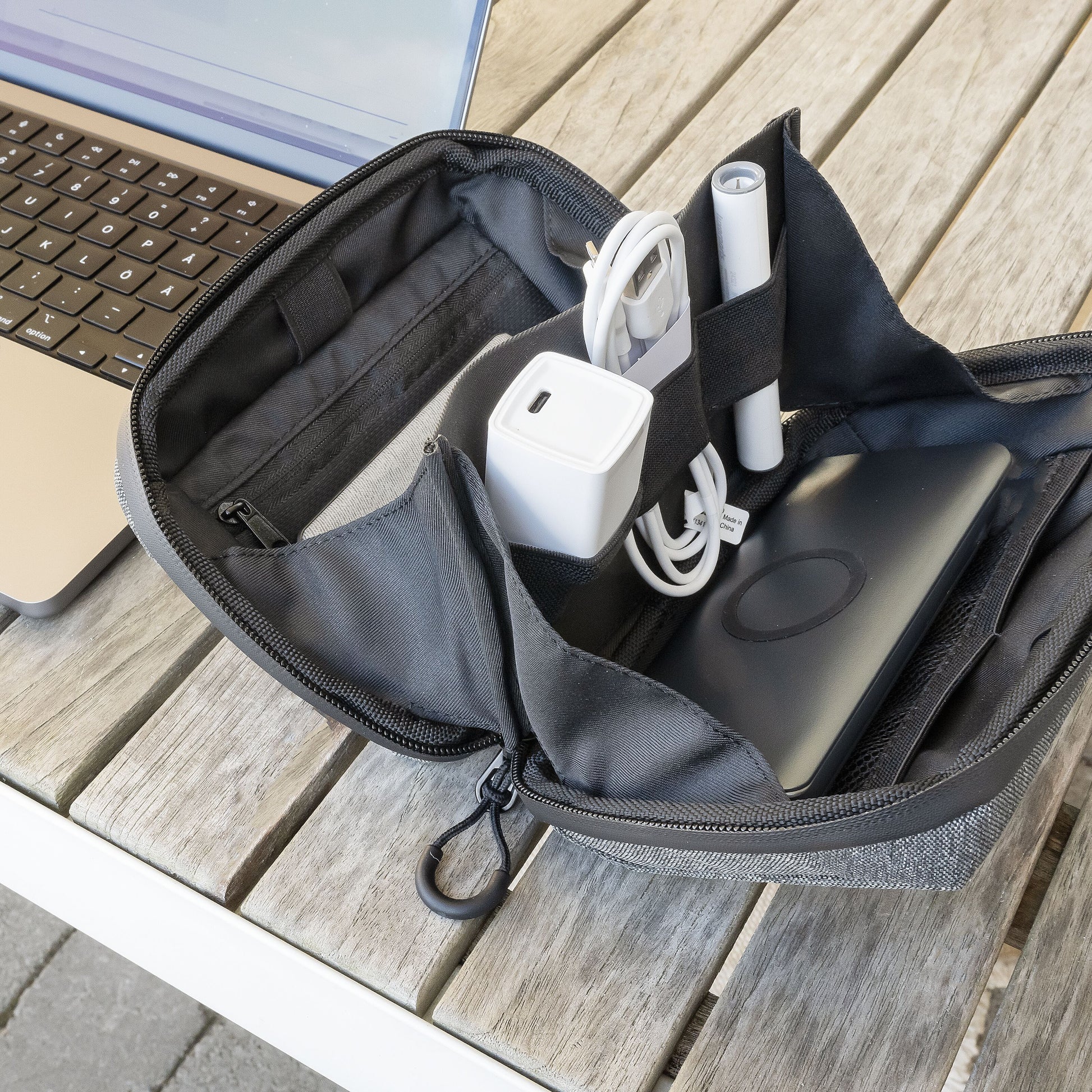 Linocell Teknologitaske i vandafvisende nylon, åben med kabler, adaptere, grå stylus og sort powerbank, laptop ved siden af.