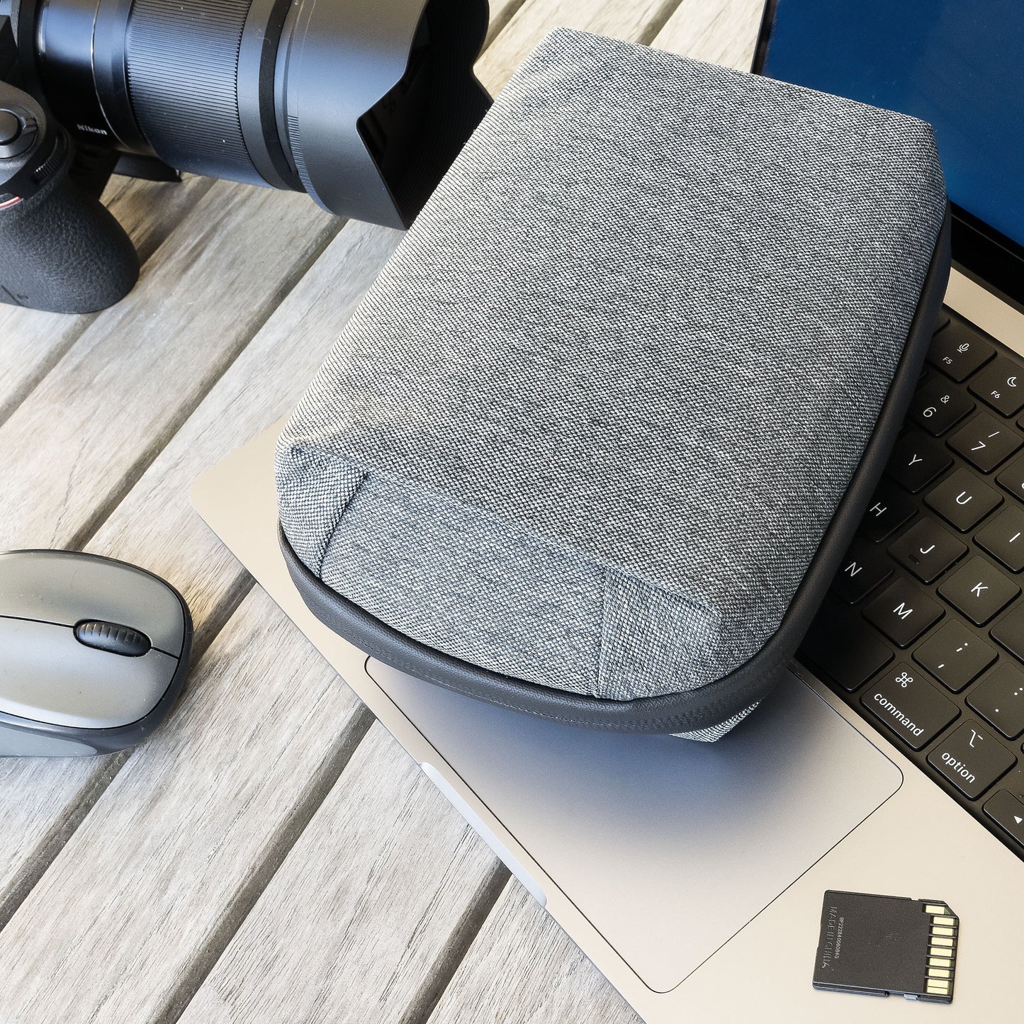 Linocell teknologitaske grå, vandafvisende nylon, ligger på laptop tastatur ved siden af trådløs mus, SD-kort og kamera.