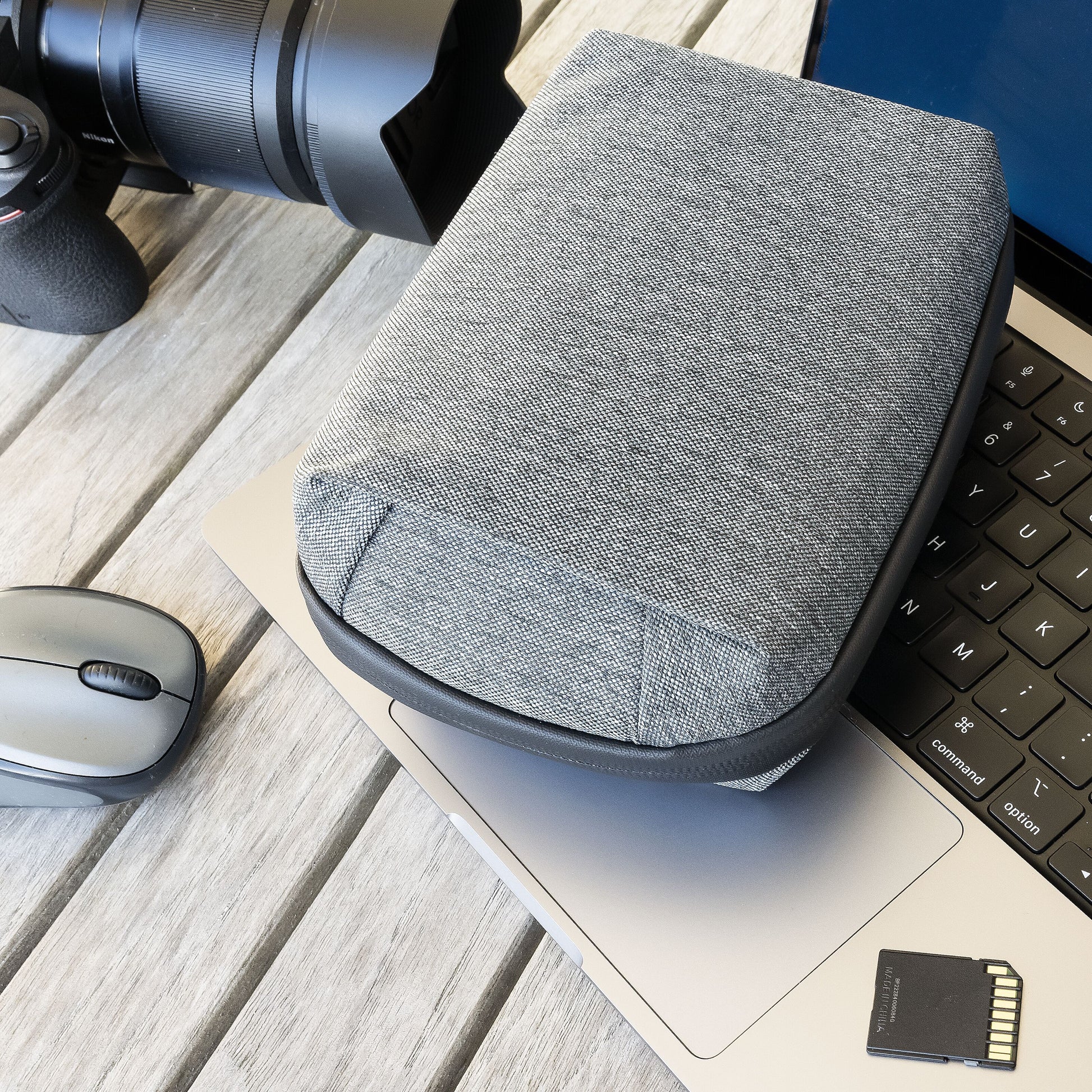 Linocell teknologitaske grå, vandafvisende nylon, ligger på laptop tastatur ved siden af trådløs mus, SD-kort og kamera.