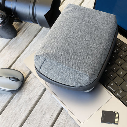 Linocell teknologitaske grå, vandafvisende nylon, ligger på laptop tastatur ved siden af trådløs mus, SD-kort og kamera.