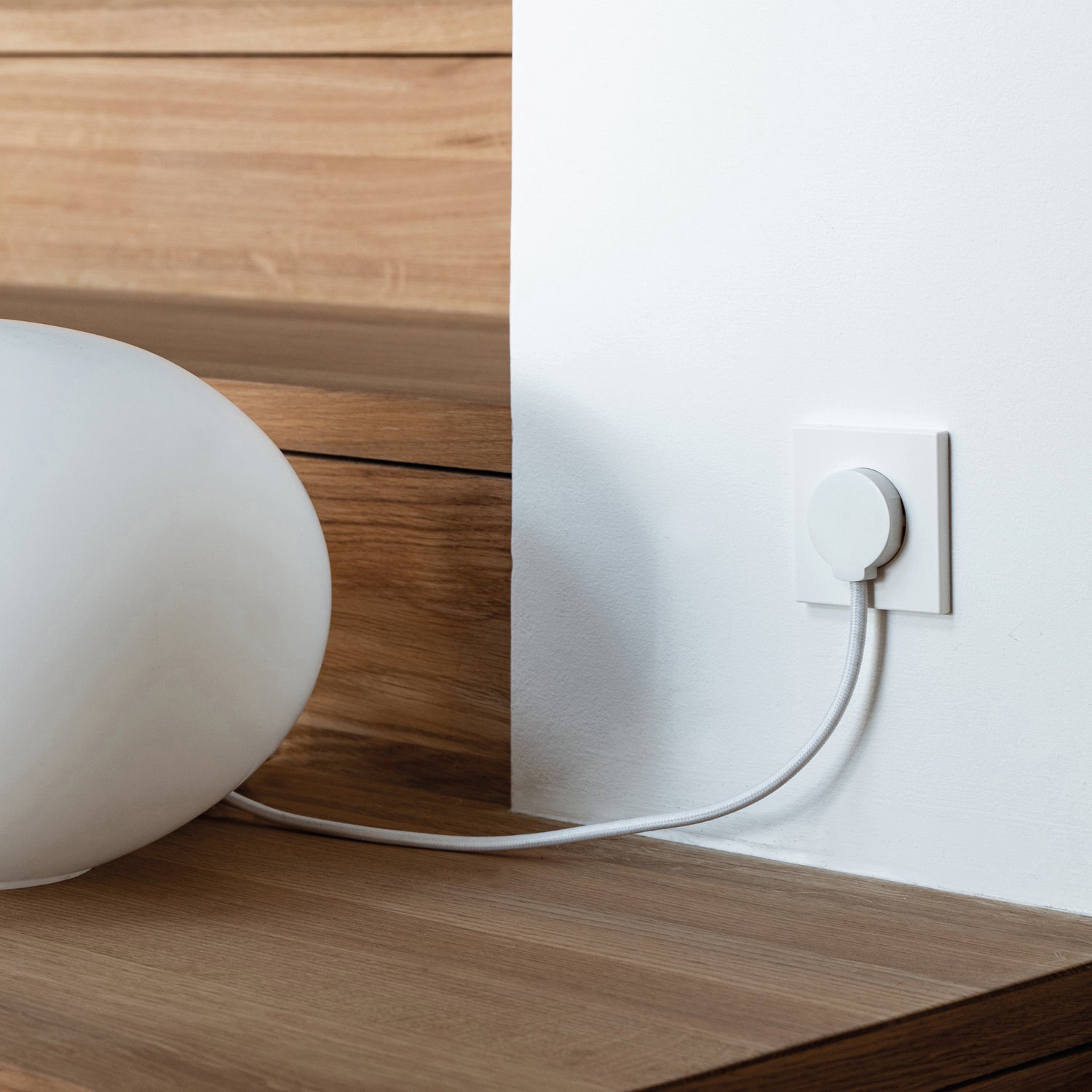 NORM stikprop Schuko Hvid med hvid ledning set tilsluttet en hvid lampe ved trætrin og hvid væg.