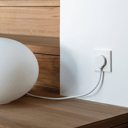 NORM stikprop Schuko Hvid med hvid ledning set tilsluttet en hvid lampe ved trætrin og hvid væg.