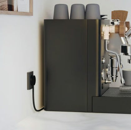Espressomaskine mørkegrå med sort NORM K stikprop med jord tilsluttet, tre grå kopper stablet ovenpå.