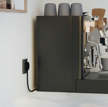 Espressomaskine mørkegrå med sort NORM K stikprop med jord tilsluttet, tre grå kopper stablet ovenpå.
