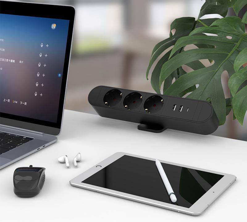 MicroConnect Multi Desktop Power Socket sort, 3 Schuko, USB-A, 2 USB-C, 30W på hvidt skrivebord ved grøn plante.