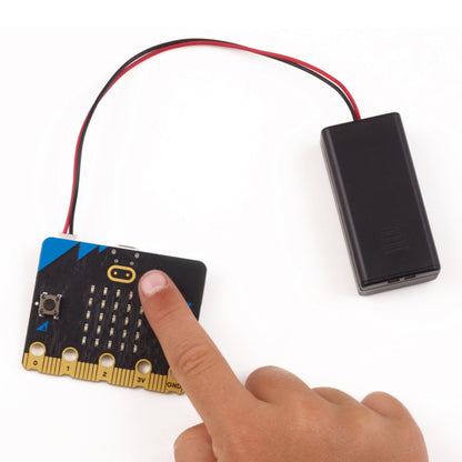 Micro:bit v2 Go med batteripakke, tilsluttet via røde og sorte ledninger, hånd trykker på knap.