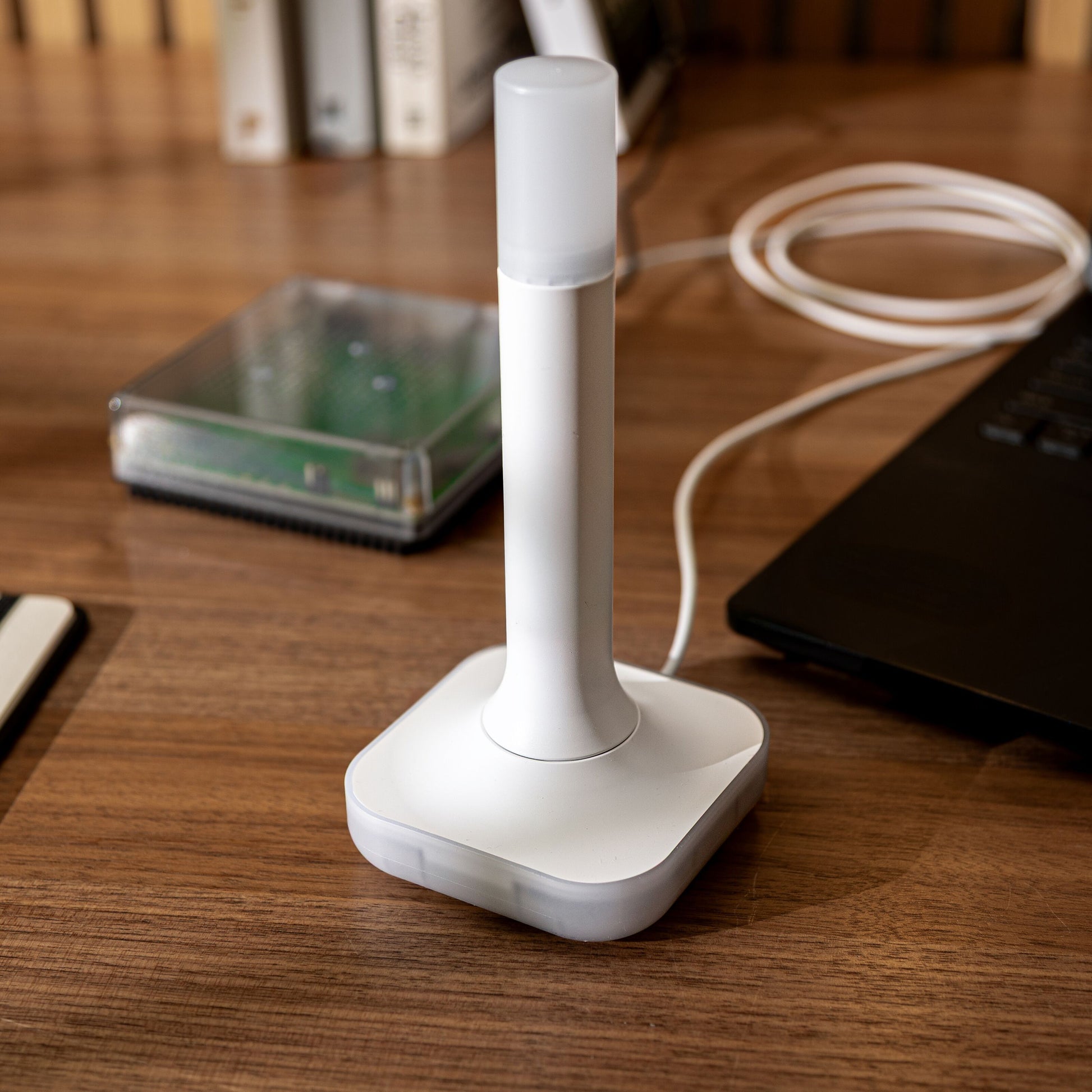 Nabu Casa Home Assistant Connect ZBT-2, firkantet base, cylinder top, hvidt kabel tilsluttet laptop på træbord.