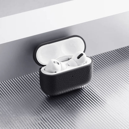 Apple AirPods Pro 3 etui i hvid i sort WOOLNUT læderetui på riflet metaloverflade ved hvidgrå kant.