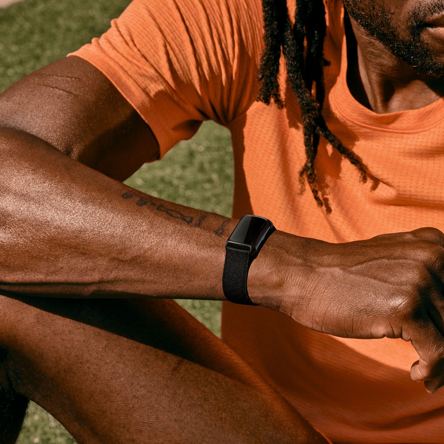 Sort Fitbit Oplad 6 aktivitetsarmbånd på håndled, orange trøje synlig, bæres udendørs.