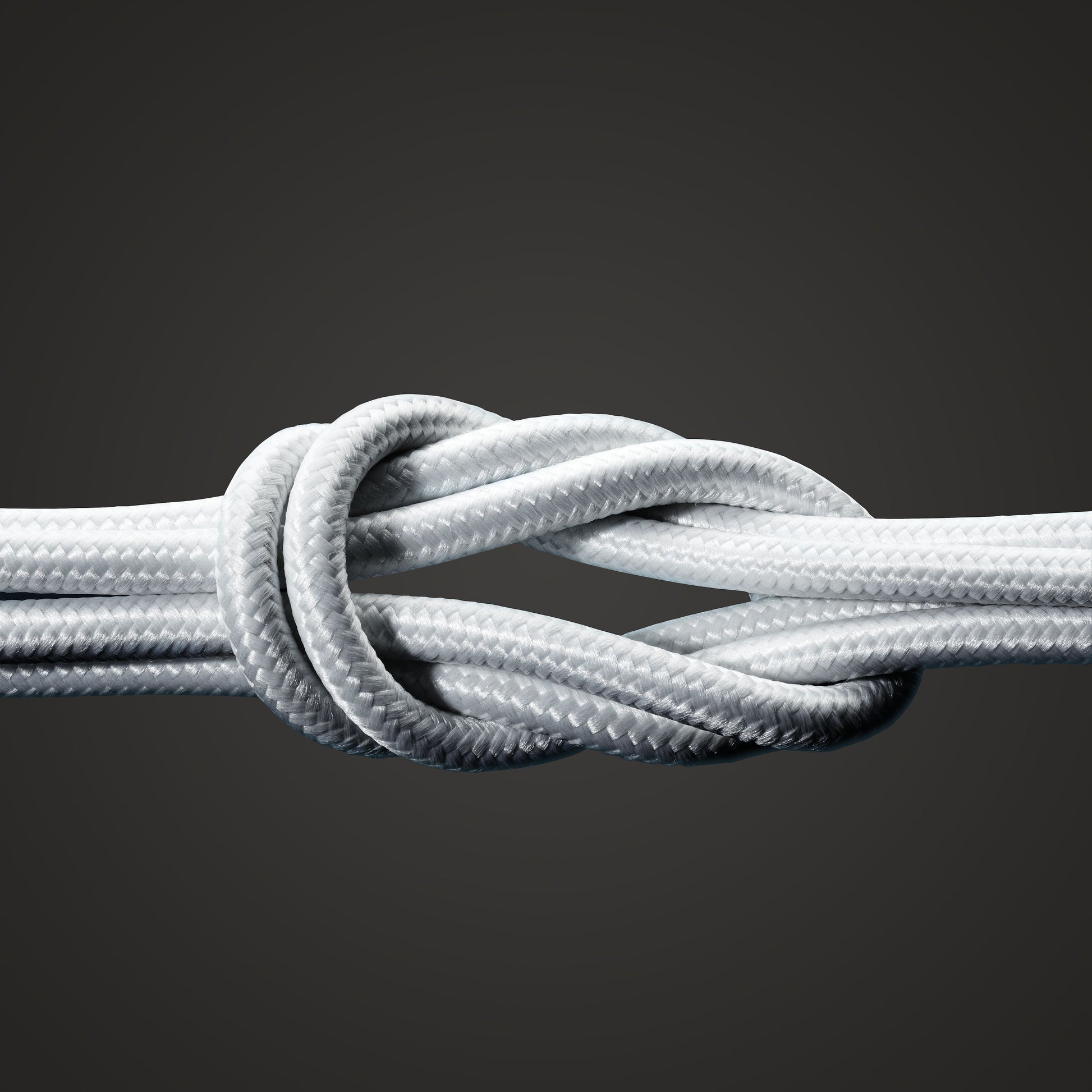 Nærbillede af to hvide flettede reb bundet i en stærk knude mod en mørk baggrund, der minder om holdbarheden og pålideligheden af det 2 m lange Linocell Kevlar USB-C til Lightning-kabel (MFi, hvid) til Apple-enheder.