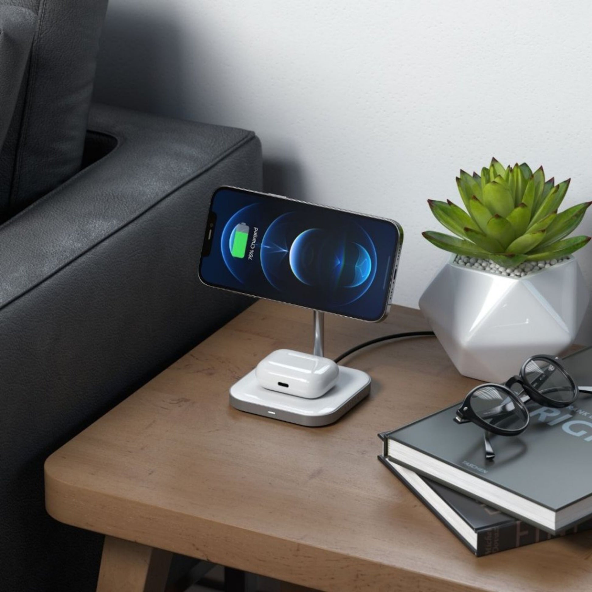 Satechi 2-i-1 magnetisk trådløs opladningsstander til smartphone og AirPods Pro på bord ved grå sofa.