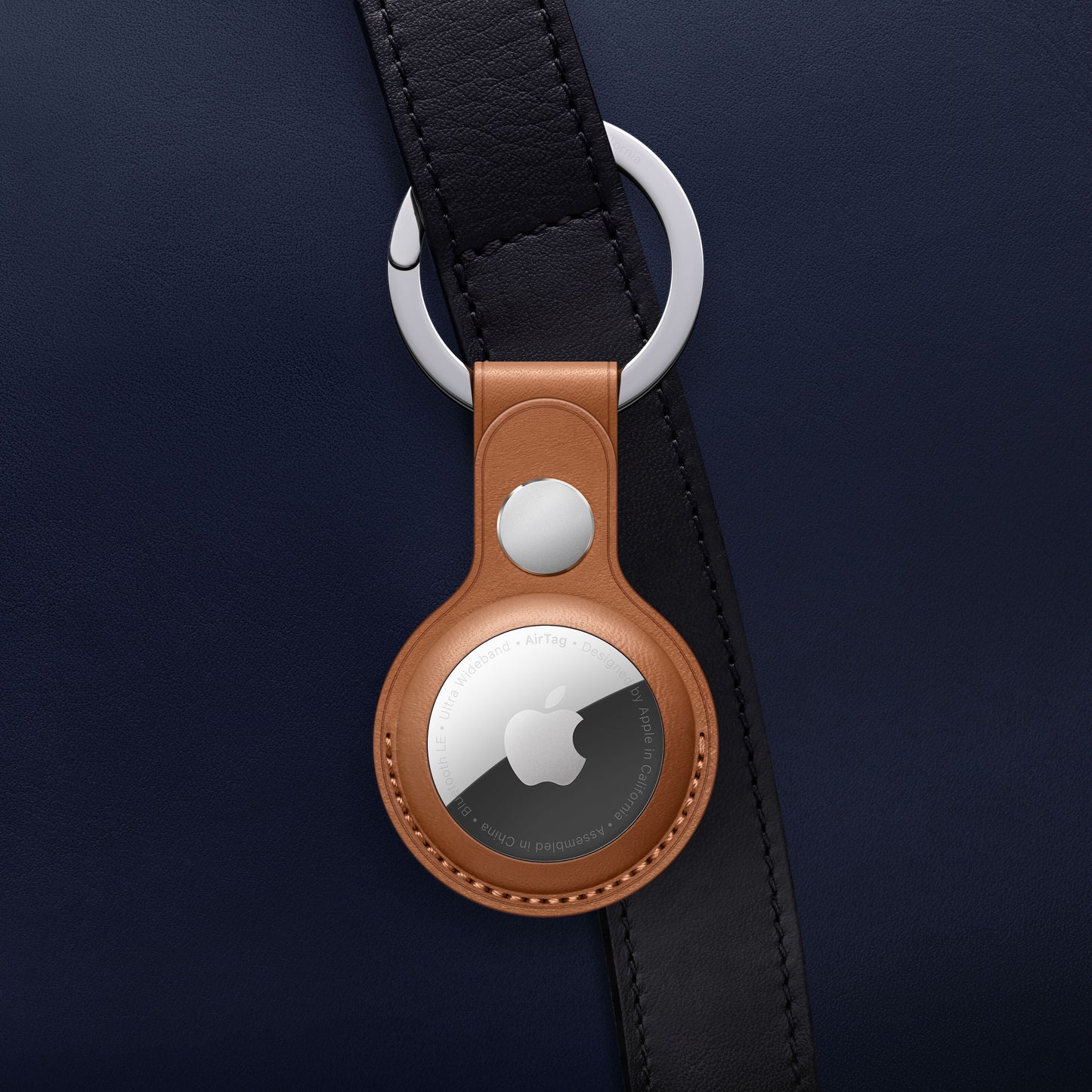 Apple AirTag i brun lædernøglering fra Apple AirTag 4-pak fastgjort til mørkeblå taskerem med sølvfarvet beslag.